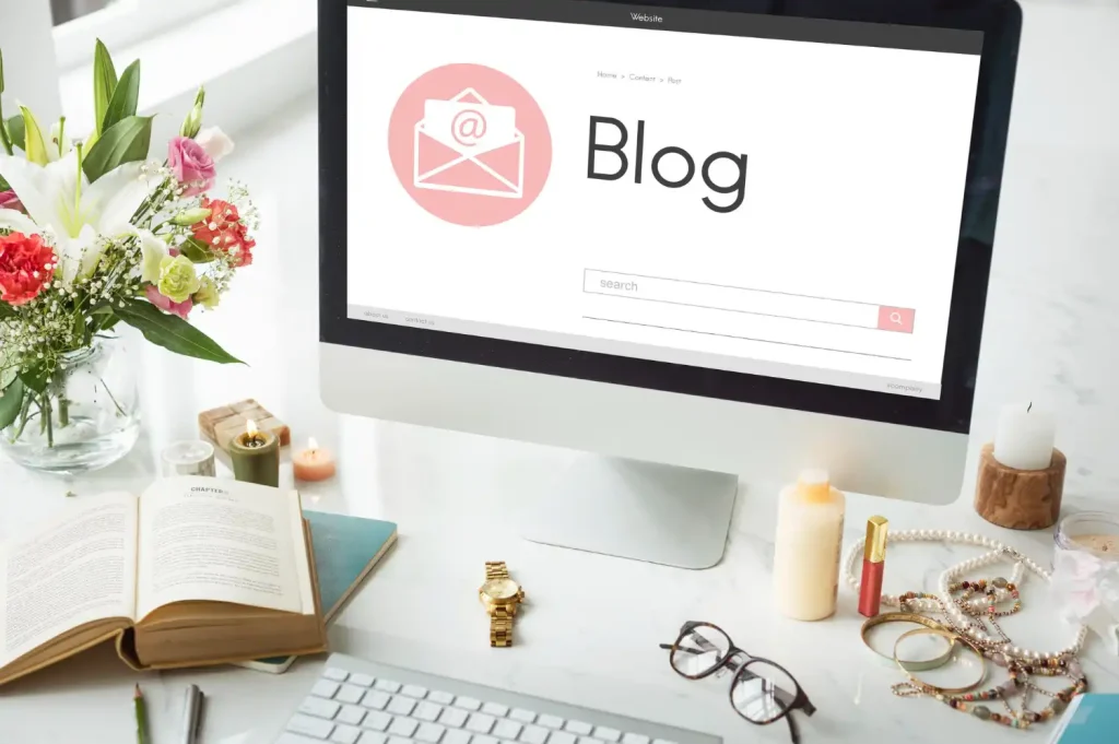 Imagem de um computador apresentando uma página de blog com conteúdo sobre estratégia de conteúdo que gera autoridade, rodeado de flores, livros, velas e acessórios de decoração em um ambiente de escritório.