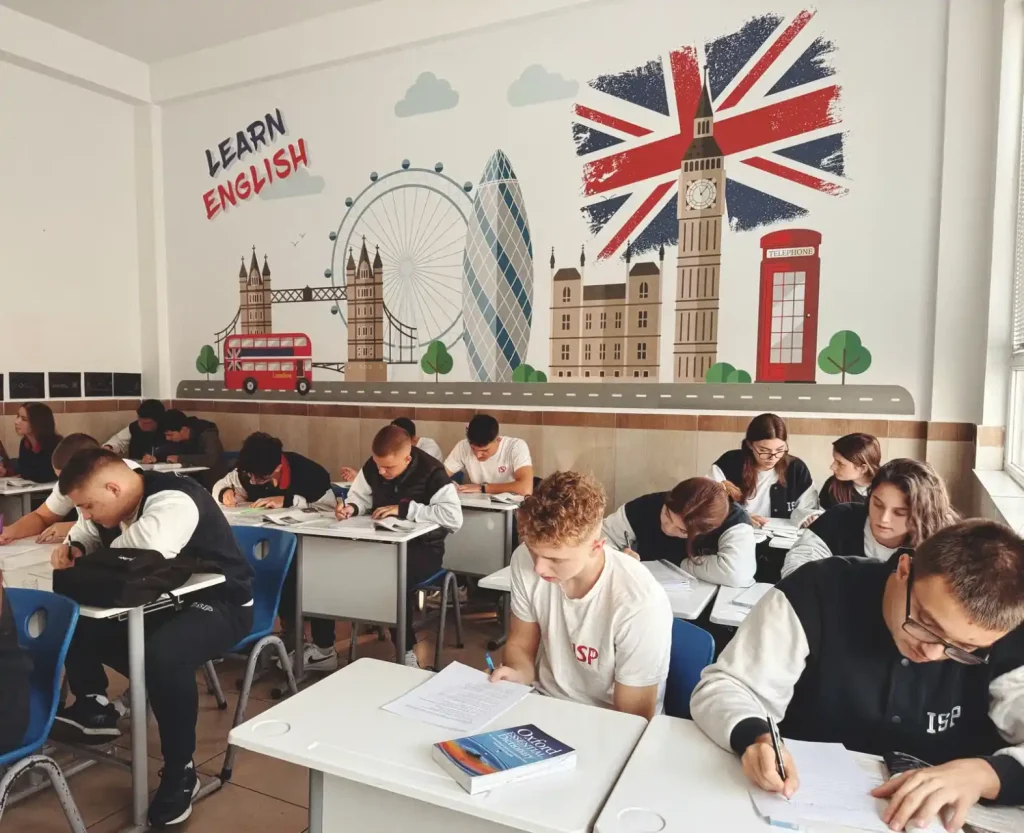 Alunos estudando inglês em sala de aula com decoração temática do Reino Unido, incluindo bandeira britânica, Big Ben e ônibus vermelho, em aula de escolas de idiomas.