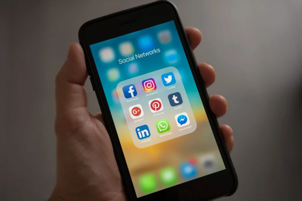 Pessoa segurando um smartphone com o aplicativo de redes sociais aberto, exibindo ícones como LinkedIn, Facebook, Instagram e Twitter, destacando uso para negócios B2B