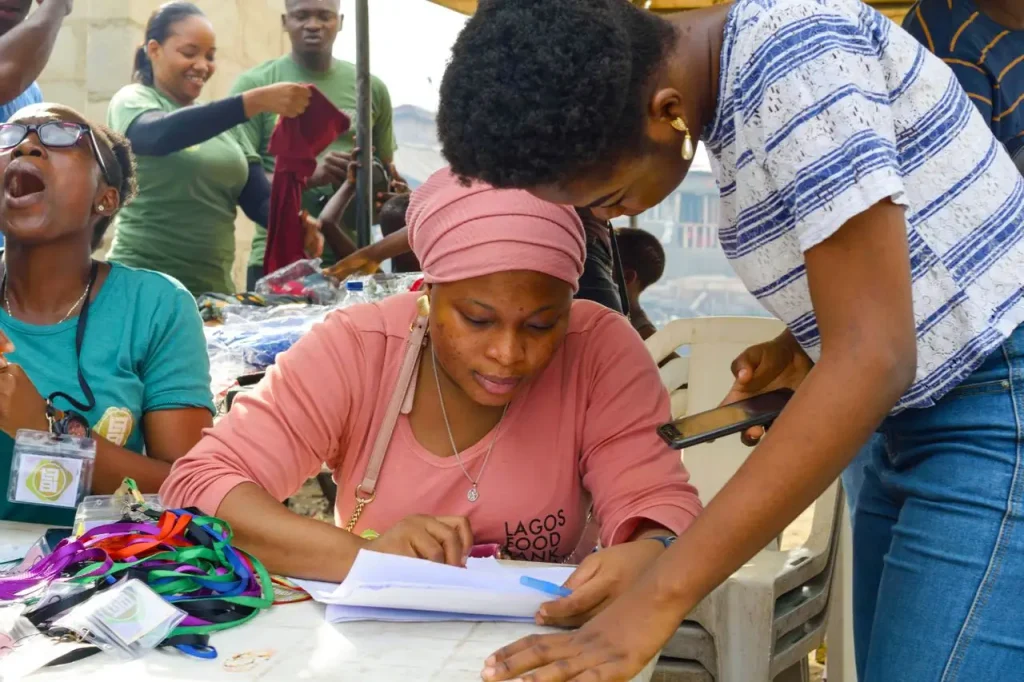 Qual o papel da assistência social na promoção da cidadania: Voluntários e participantes em um trabalho comunitário, com pessoas preenchendo e organizando documentos em uma mesa com materiais coloridos, em ambiente de atendimento social.