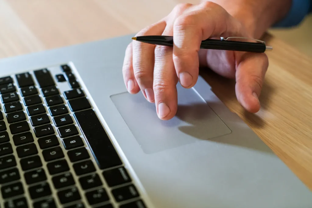 Por que a era da assinatura vitalícia acabou: o que muda quando o cliente pode cancelar em 1 clique: Mão usando um laptop com o dedo em um touchpad, em uma cena que remete a controle de assinatura e cancelamento online com um clique.