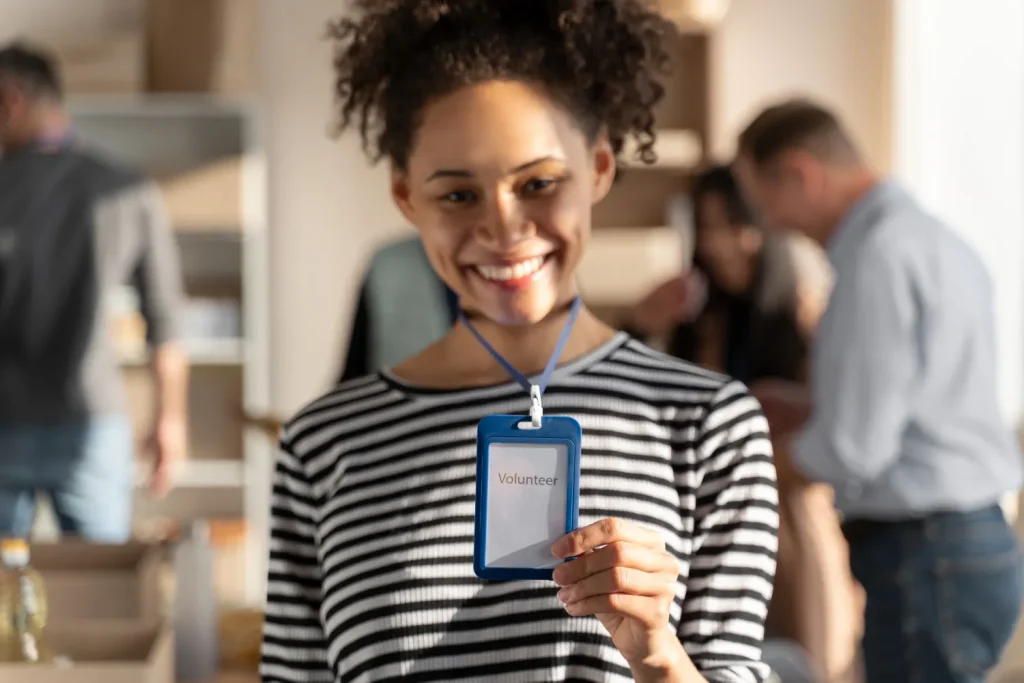 Jovem sorrindo em evento corporativo, segurando uma Credencial com cordão: Vantagens e aplicações para eventos, empresas e instituições, com crachá azul preso ao pescoço.