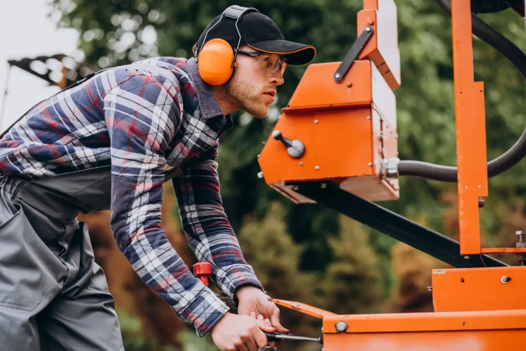 Peneira vibratória inclinada: Como funciona e onde utilizar na indústria: Técnico usando EPI opera uma peneira vibratória inclinada em ambiente industrial ao ajustar o equipamento laranja para separação de materiais