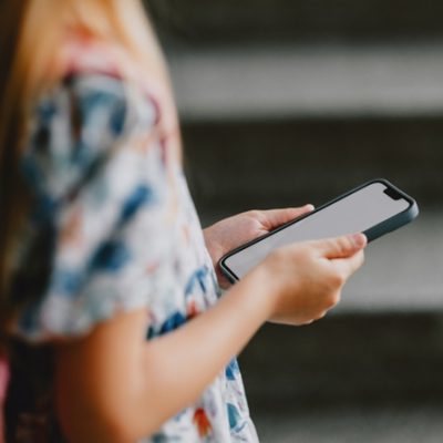 Young girl with a backpack holding a smartphone. Back to school concept showcasing technology and education. Créditos: FreshSplash/iStock
