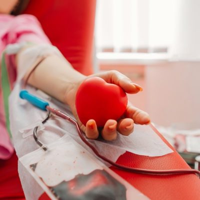 Young woman making blood donation in hospital. A woman donates blood while holding a red heart. Blood donation.