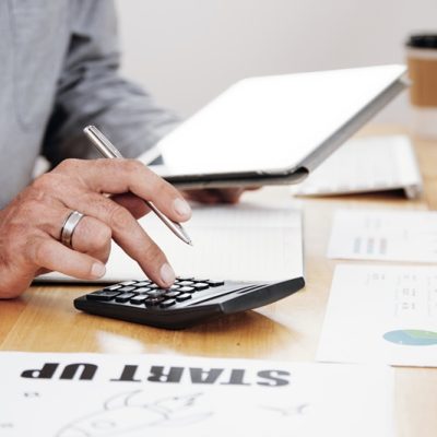 Close-up of businessman counting the profit of the company and using digital tablet at office desk