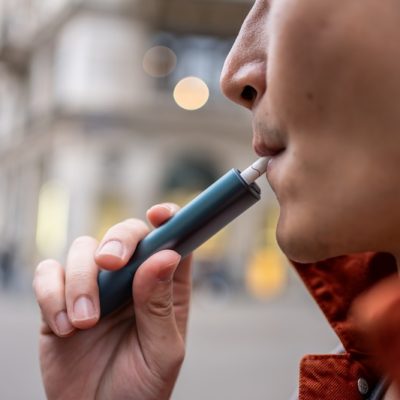 Close up of a man vaping with electronic cigarette outdoor on street. Attractive handsome male tourist travel alone on street, enjoy blowing the dense smoke out during walking in city town for holiday - Estudos já apontam alterações celulares associadas ao vape que podem favorecer o desenvolvimento de câncer de boca
Divulgação Envato
