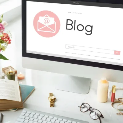 Imagem de um computador apresentando uma página de blog com conteúdo sobre estratégia de conteúdo que gera autoridade, rodeado de flores, livros, velas e acessórios de decoração em um ambiente de escritório.