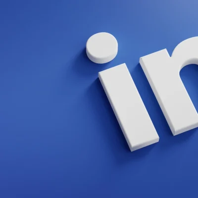 Imagem com fundo azul e o texto em 3D “IN”, com um ícone circular branco sobre o “I”, remetendo a uma ideia de entrada/inscrição e comunicação digital, ideal para ilustrar engajamento em comunidades no LinkedIn e desempenho além do feed.