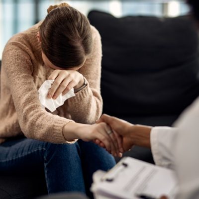 Sad woman crying while holding hands with her psychotherapist at doctor's office. Magnific