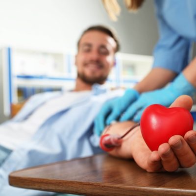 Young man making blood donation in hospital, focus on hand