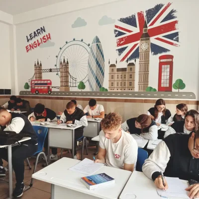 Alunos estudando inglês em sala de aula com decoração temática do Reino Unido, incluindo bandeira britânica, Big Ben e ônibus vermelho, em aula de escolas de idiomas.