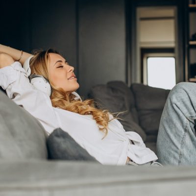 Young woman listening to music in earphones in her appartment - Foto: Magnific