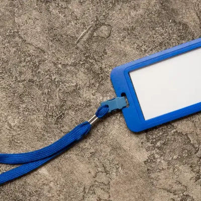 Crachá de identificação azul com presilha de cordão, mostrando a área branca para personalização, em fundo de concreto. Ideia para Fabricante de crachá: Como escolher uma empresa para produzir crachás personalizados.