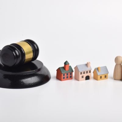 Judge gavel with miniature houses and wooden family figures on white background. Concepts of property disputes, inheritance rights, housing ownership, and legal decisions affecting family real estate assetsCréditos: Muhammad Labib Adilah/iStock.