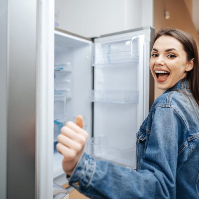 Young attractive woman choosing refrigerator in hypermarket close up