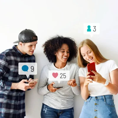 Três jovens conversam e interagem enquanto usam celular, com ícones de curtidas e comentários sobrepostos na imagem, representando Marketing de Comunidade: Como Construir Audiências Fiéis Fora dos Algoritmos.