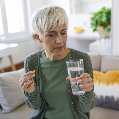 Senior woman takes pill with glass of water in hand. créditos: Freepik