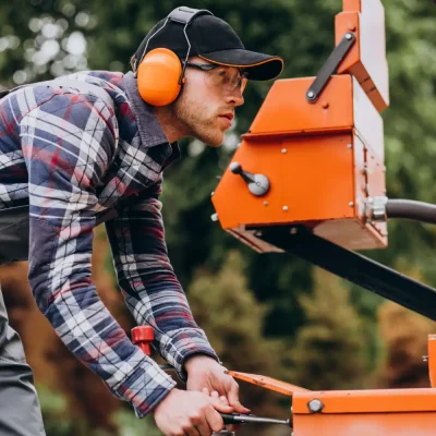 Peneira vibratória inclinada: Como funciona e onde utilizar na indústria: Técnico usando EPI opera uma peneira vibratória inclinada em ambiente industrial ao ajustar o equipamento laranja para separação de materiais