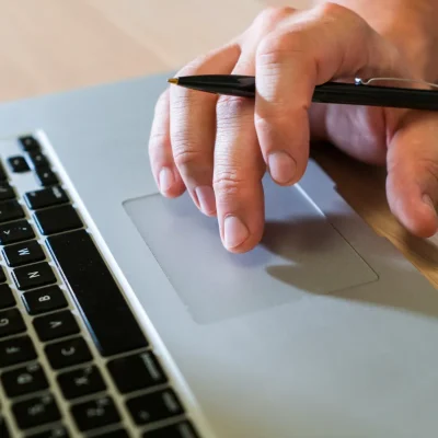 Por que a era da assinatura vitalícia acabou: o que muda quando o cliente pode cancelar em 1 clique: Mão usando um laptop com o dedo em um touchpad, em uma cena que remete a controle de assinatura e cancelamento online com um clique.