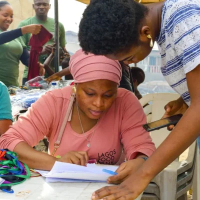 Qual o papel da assistência social na promoção da cidadania: Voluntários e participantes em um trabalho comunitário, com pessoas preenchendo e organizando documentos em uma mesa com materiais coloridos, em ambiente de atendimento social.