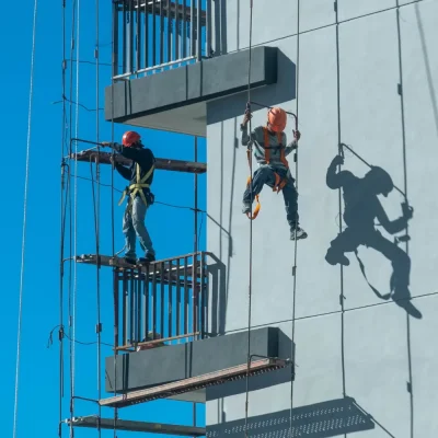 Trabalho em altura acima de 2 Metros: Cuidados, equipamentos e normas de segurança: Equipe realiza trabalho em altura na fachada de um prédio, usando arnês e sistema de acesso para manutenção, com atenção à segurança e equipamentos de proteção.